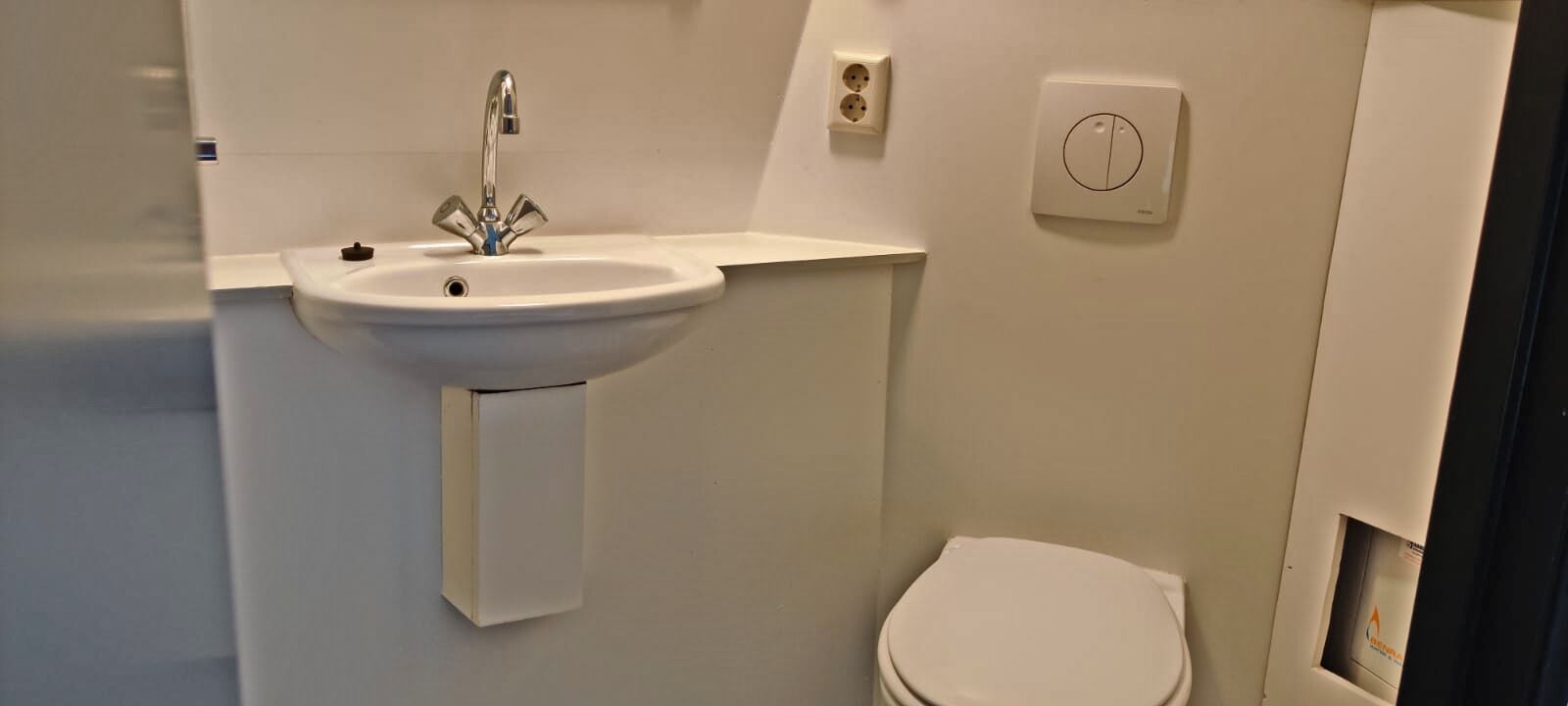 A bathroom with a white sink, a toilet, and a wall-mounted electrical outlet.