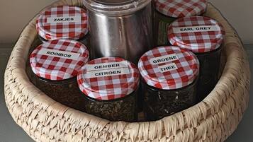 A woven basket containing jars with checkered lids labeled with names like "ZAKJES," "EARL GREY," and "GROENE THEE."
