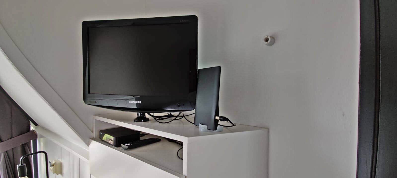 Et Samsung TV ophængt på en hvid væg i et rum med en trappe.