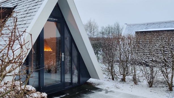 Ein modernes Haus mit einem dreieckigen Dach und einer Glastür, die zu einem beleuchteten Innenraum führt.