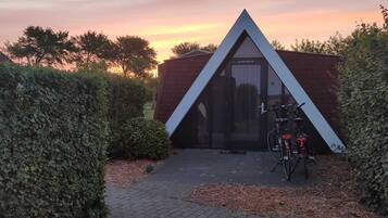 A modern building with a triangular roof and a glass door, surrounded by hedges and a bicycle parked in front.