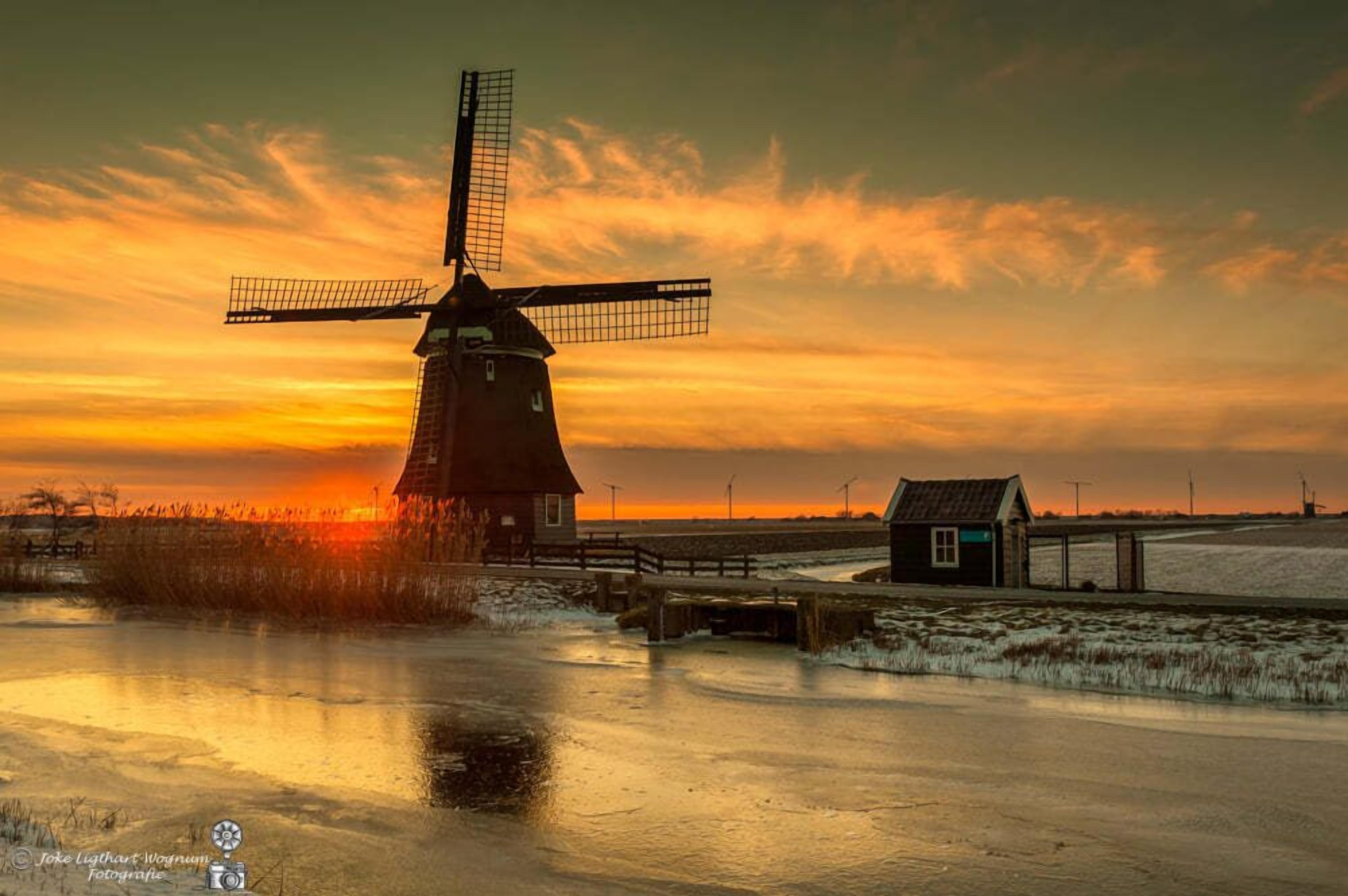A windmill by a frozen body of water at sunset.