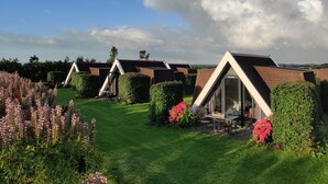 A row of modern, triangular-roofed cottages with a grassy lawn and flower beds in the foreground. - Hotelhuisje Warmenhuizen #D (Warmenhuizen)