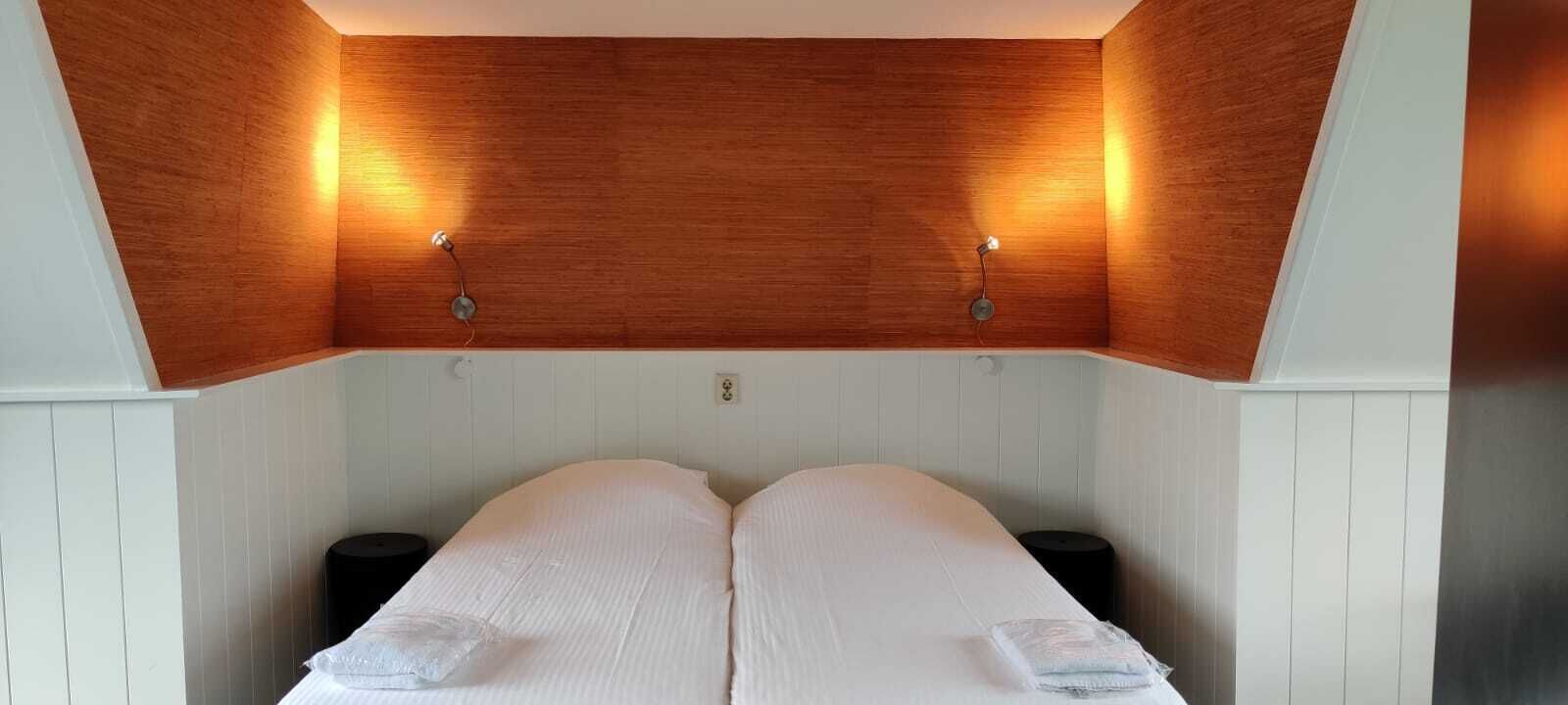 A bedroom with a wooden ceiling, two bedside tables, and a bed with white linens.