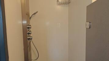 Een kleine, afgesloten douchecabine met een handdouche en een bedieningspaneel aan de wand.