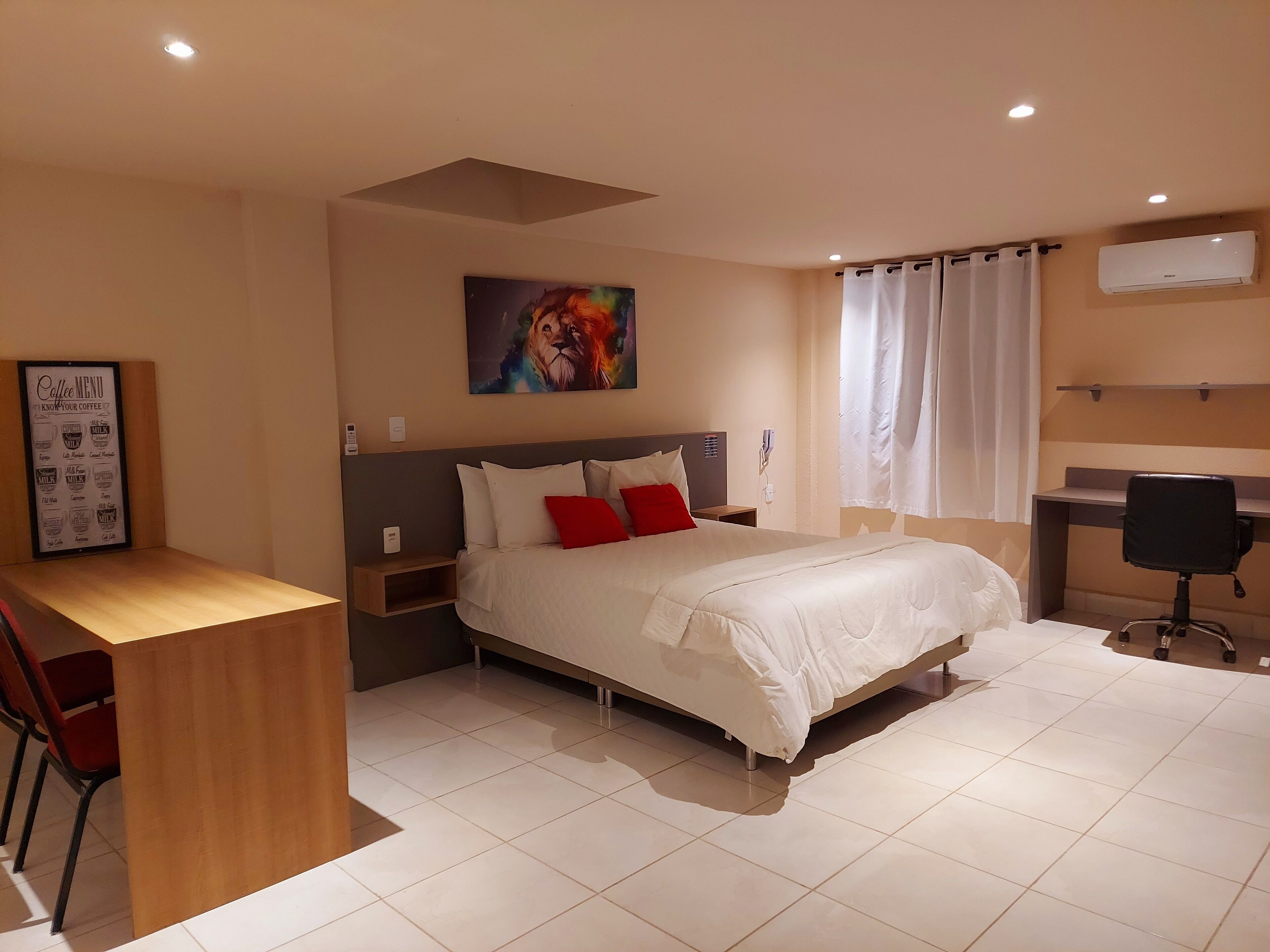 Una habitación de hotel con cama, escritorio, silla, un cuadro y un equipo de aire acondicionado.