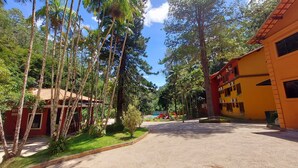 A street lined with tall trees and a building with a red roof. - Hotel Vila Suíça 1818 (Nova Friburgo)
