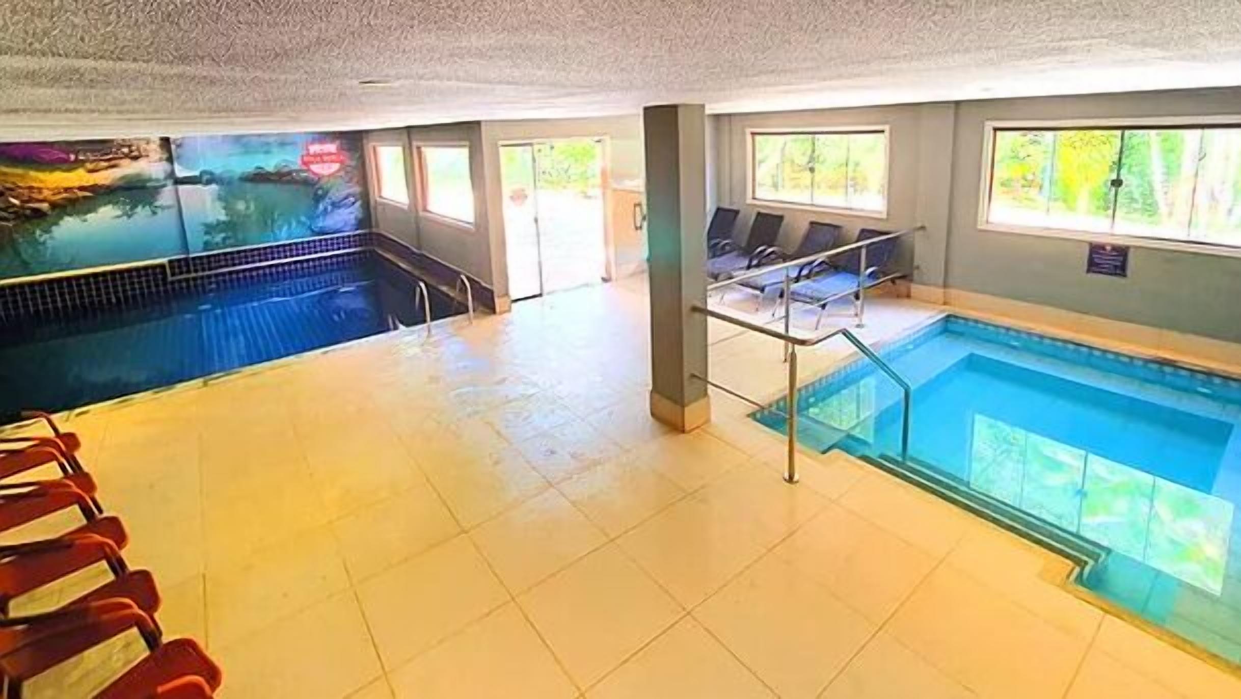 Una piscina interior con agua cristalina, suelo de baldosas y algunas sillas de descanso.