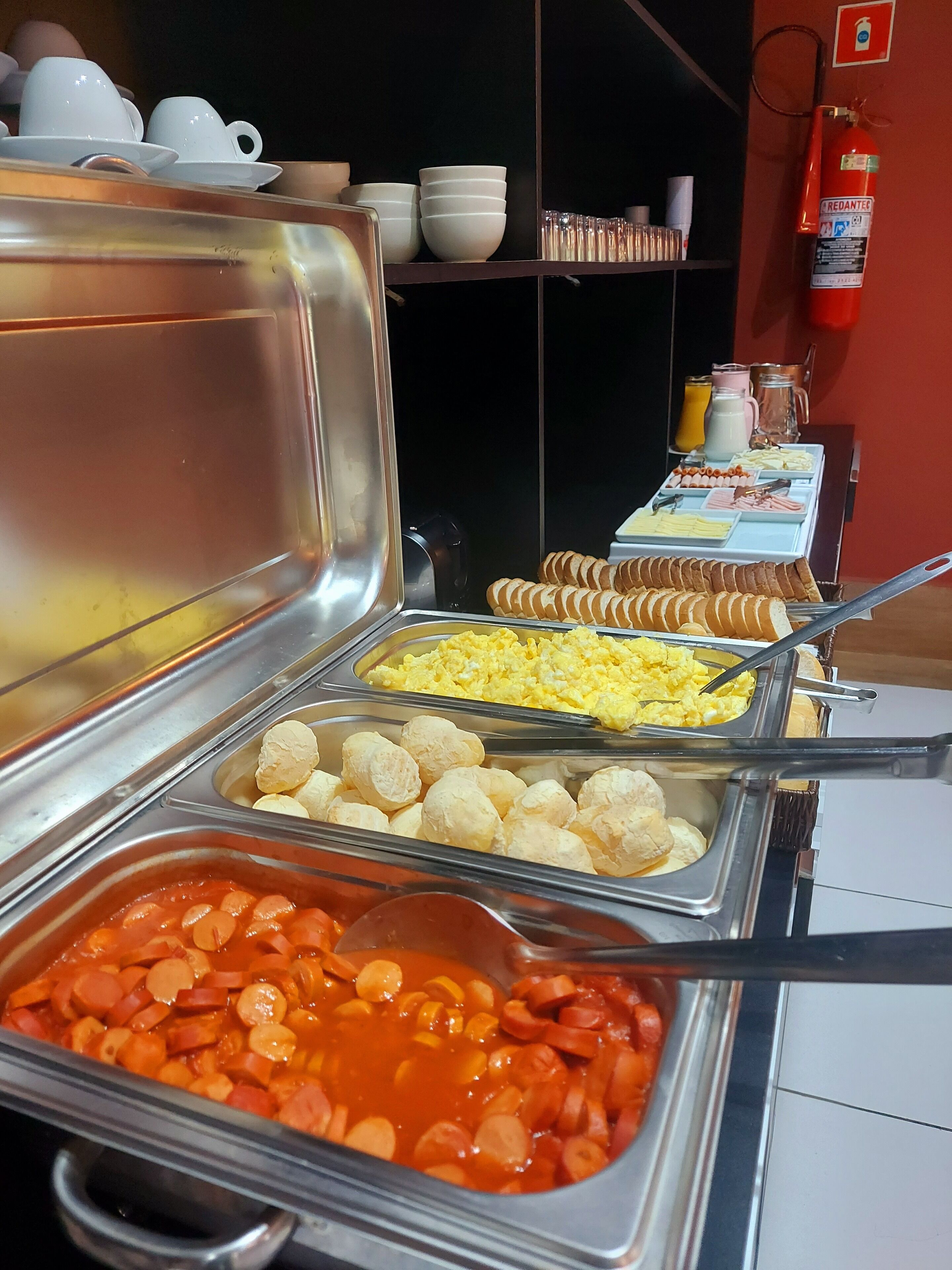 Un buffet con diversi piatti, tra cui uova strapazzate, salsiccia e panini.