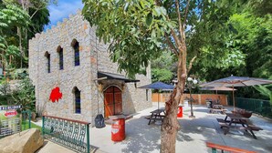 A stone building with a wooden door and windows, surrounded by greenery and outdoor seating areas. - Hotel Vila Suíça 1818 (Nova Friburgo)