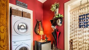 Ein Waschbereich mit Waschmaschine, kleinem Kühlschrank und einem Regal mit Hüten und einer Lampe.