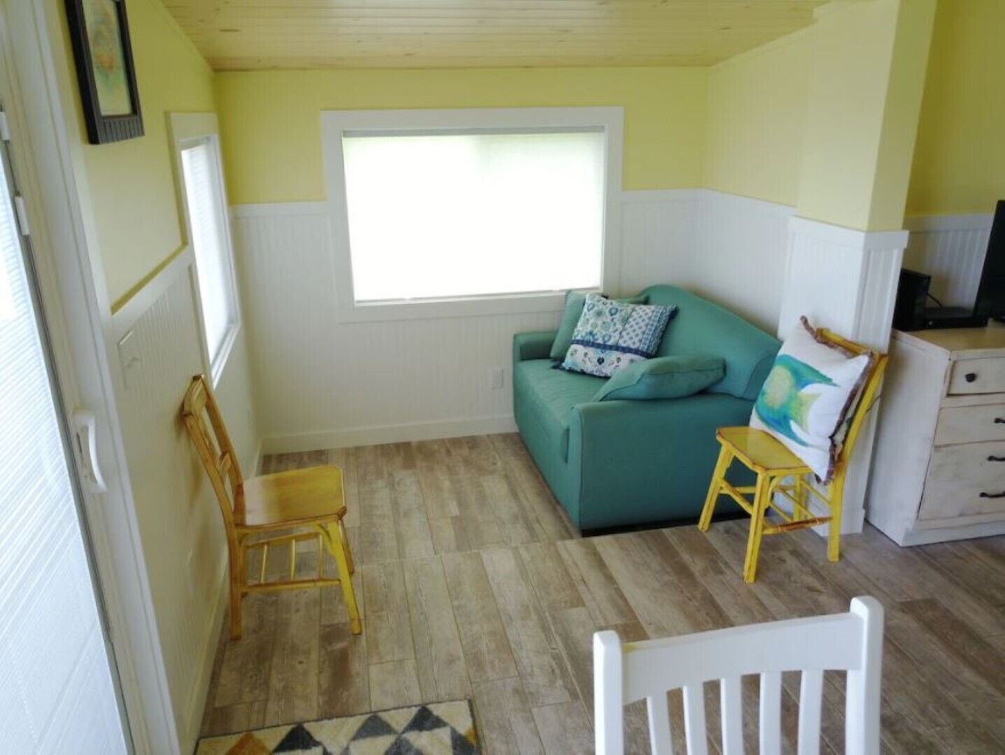 A compact living space with a green sofa, a wooden chair, a small table, and a window providing natural light.