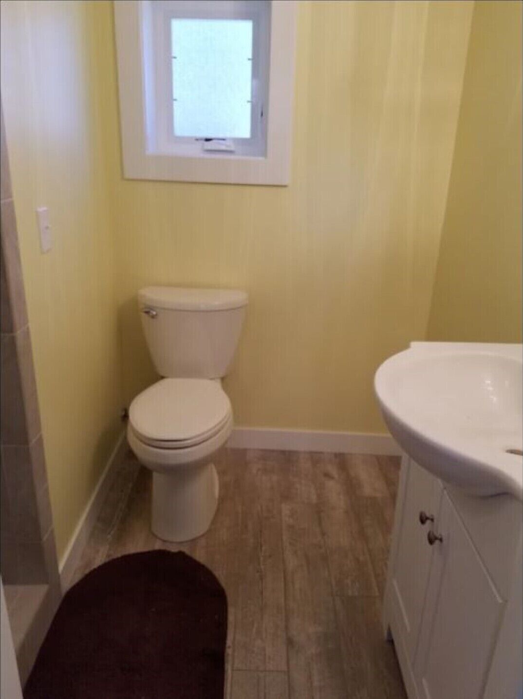 A small bathroom with a toilet, a sink, and a window above the toilet.