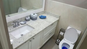 Une salle de bain avec un lavabo, un miroir, des toilettes et un récipient bleu posé sur le comptoir.