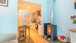 A cozy kitchen with a wood-burning stove, a dining area with a table and chairs, and a visible washing machine. - 1 bedroom accommodation in Ulva Ferry (Ulva Ferry)