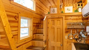 A wooden cabin interior with a kitchen area, including a sink, cabinets, and a window overlooking the outside. - Boutique Tiny Home! Pikes Peak Views, HOT TUB, fire pit, & cozy vibes. (Woodland Park)