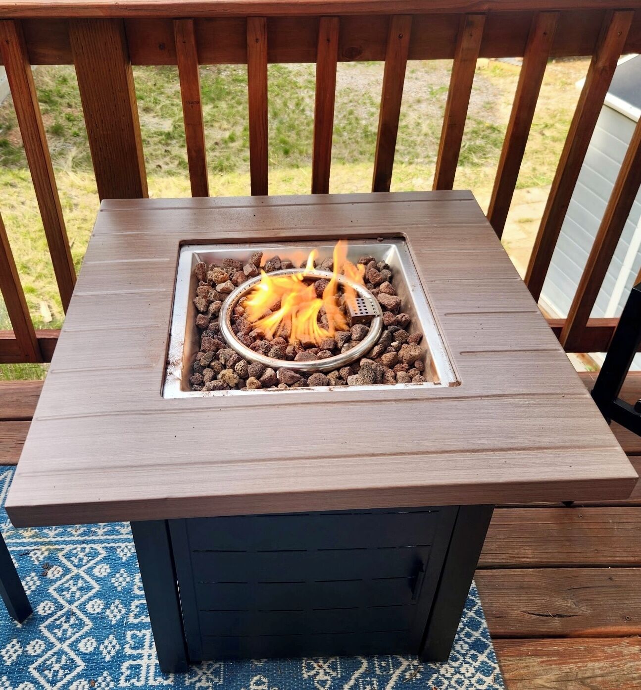 A square outdoor table with a metal fire pit in the center.