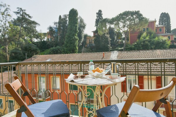 A balcony with a table set for breakfast, including bread, a bottle, and cups.