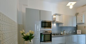 A modern kitchen with white cabinetry, a built-in oven, and a microwave. There is a vase with flowers on the table.