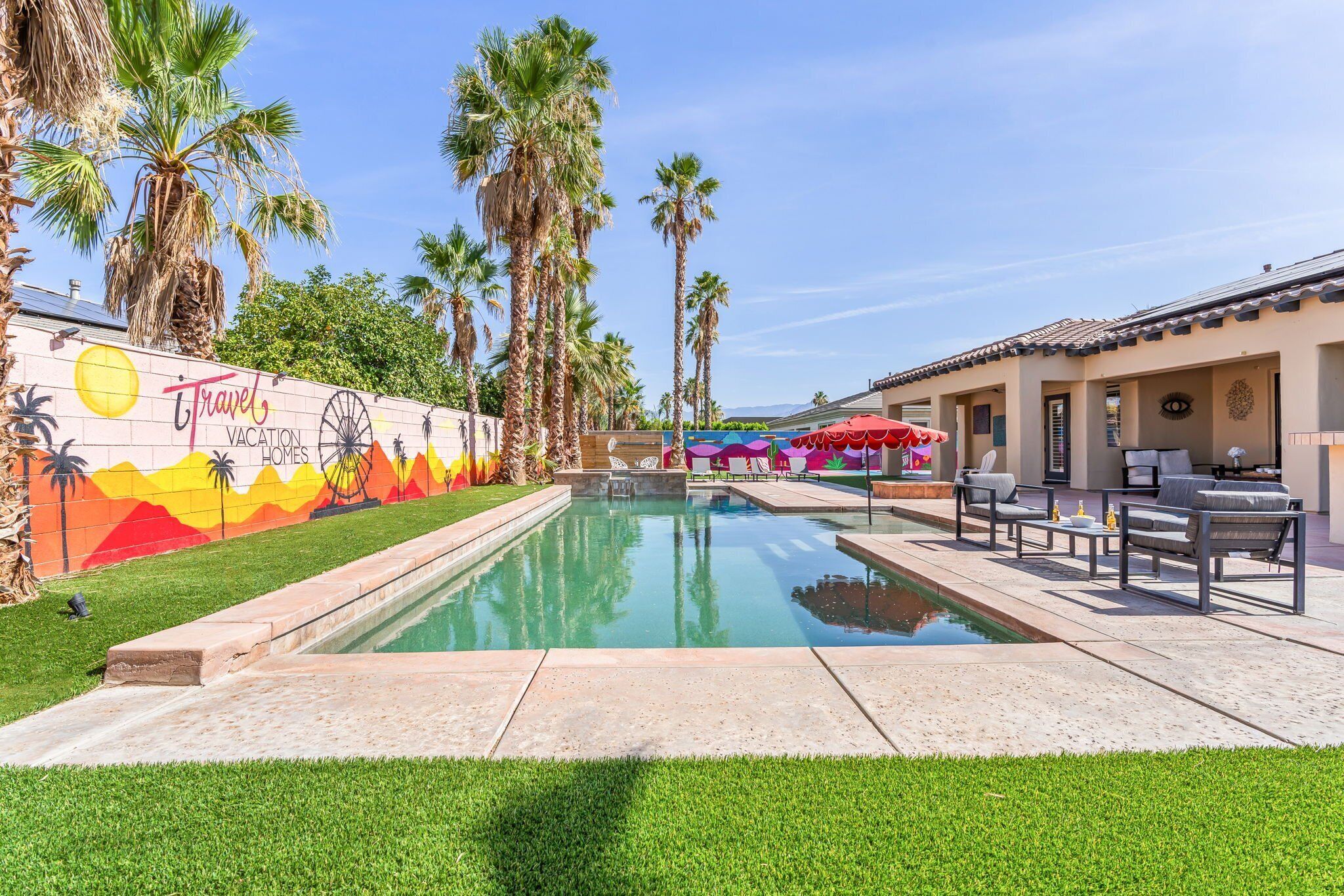 Une piscine agrémentée d’une fresque murale, de palmiers et d’un espace salon extérieur.