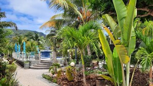 A tropical garden pathway leading to a seating area with blue umbrellas. - Cabanes des Anges Guest House (La Digue)