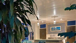 A well-lit indoor area with a stone counter, green chairs, and large potted plants. - Cabanes des Anges Guest House (La Digue)