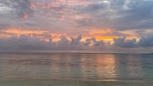 A beach with a sunset and clouds over the ocean. - Cabanes des Anges Guest House (La Digue)