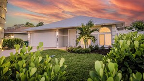 A modern house with a garage, a well-maintained lawn, and a palm tree. - Coastal Beachy 3+/2, Pool, 5 Bikes, Near Beach, Pet Friendly, Sleeps 8+ (Naples)