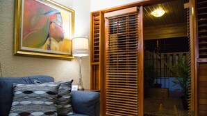 A living room with a blue sofa, patterned cushions, a framed painting, a floor lamp, and a wooden door leading to an outdoor area with a potted plant. -   Luxury Log Cabin with picturesque Mountain view (Kingston)