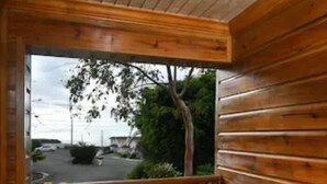 A wooden balcony with a chair and a table, overlooking a street and greenery. -   Luxury Log Cabin with picturesque Mountain view (Kingston)
