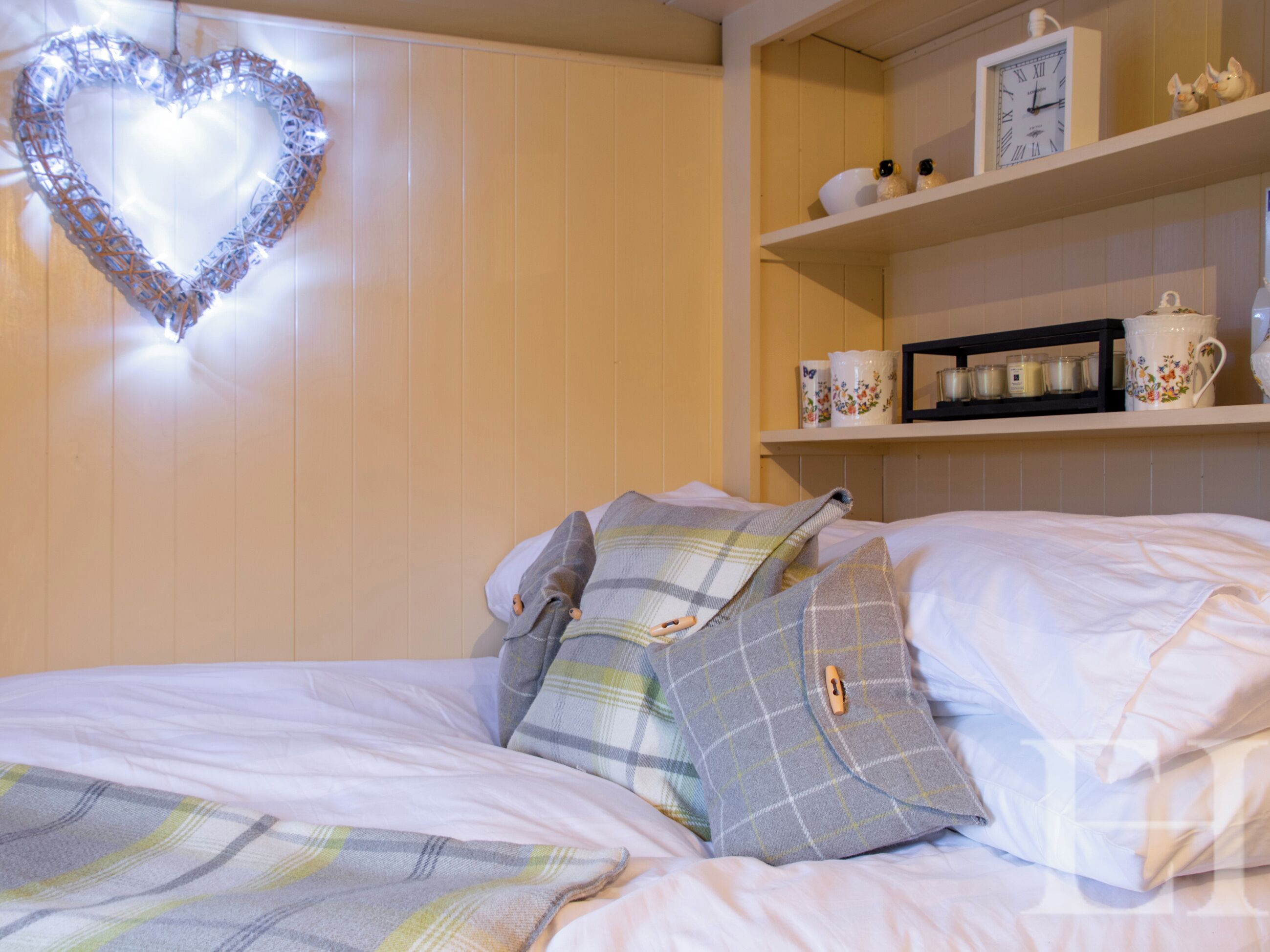 A neatly made bed with plaid pillows and a heart-shaped light decoration on the wall.