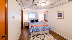 Un dormitorio con cama, lámparas de noche, una ventana, un cuadro enmarcado y una puerta de madera.