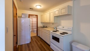 Una cocina compacta con armarios blancos, un refrigerador, una estufa y un lavamanos.