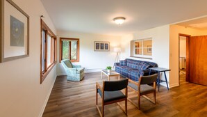 Amplia sala de estar con piso de madera, un sofá de tapicería azul a cuadros, un sillón azul claro y una mesa de centro de madera.