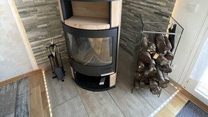 Un poêle à bois moderne, doté d’une cheminée noire, d’une étagère en bois et d’un support métallique pour les bûches.