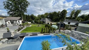 Une piscine rectangulaire hors sol, dotée d’un escalier, entourée de murs en pierre et de verdure.