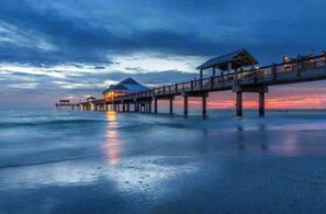 Un hotel frente al mar con un muelle que se adentra en el océano, con varias cabañas sobre el agua y un paseo techado.