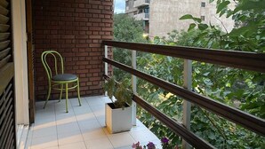 A balcony with a green chair, a potted plant, and a view of surrounding buildings and greenery. - Portillo Apartments (Mendoza)