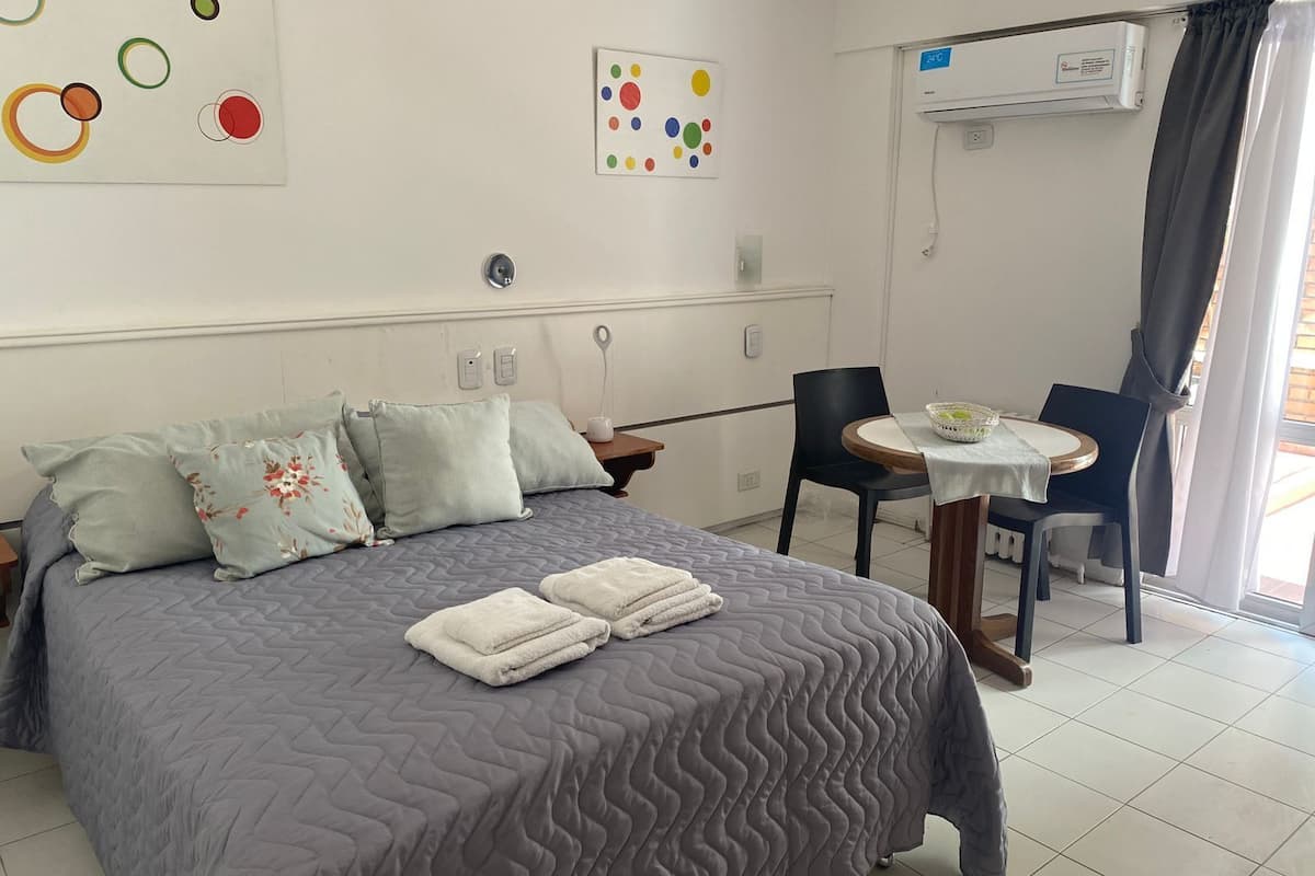 A neatly arranged bedroom with a bed, pillows, a bedside table, a chair, and a small table with a basket.