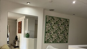 A modern living room with a beige sofa, a white chair, and a kitchen area with a white countertop. - Portillo Apartments (Mendoza)