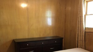 Une chambre avec une armoire en bois, un lit doté d’un matelas à motifs floraux et une fenêtre avec des rideaux.