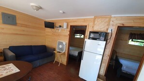 Habitación pequeña con sofá azul, una mesita, refrigerador blanco, microondas y ventilador de techo.