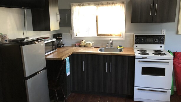 A compact kitchen with dark cabinets, a white stove, a sink, and a window with curtains.