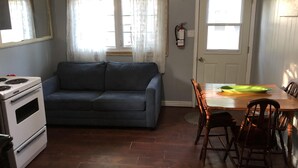 A compact living space with a kitchenette, a sofa, a dining table with chairs, and a door with a window.
