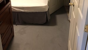 Een slaapkamer met een bed, een houten dressoir, een deur en een lichtschakelaar aan de muur.