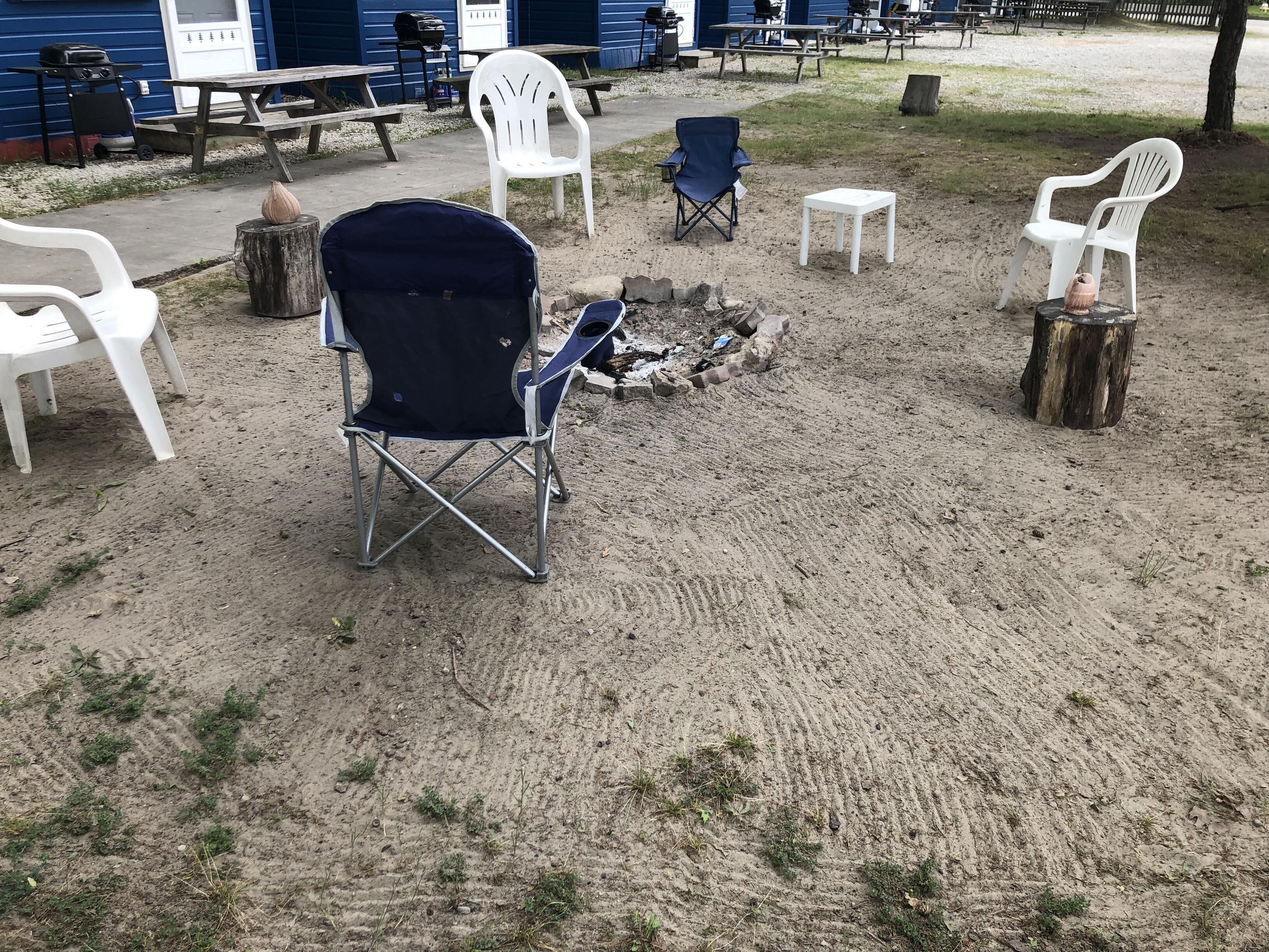 Un espace extérieur aménagé avec des sièges, un foyer, des chaises en plastique blanches et une chaise pliante bleue.