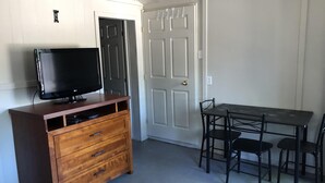 Une pièce comprenant une commode en bois, un téléviseur à écran plat, une table à manger avec quatre chaises et une porte blanche dotée d’une poignée.