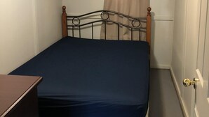 Une petite chambre avec un lit simple, une tête de lit en bois, une table de chevet et une fenêtre avec des rideaux.