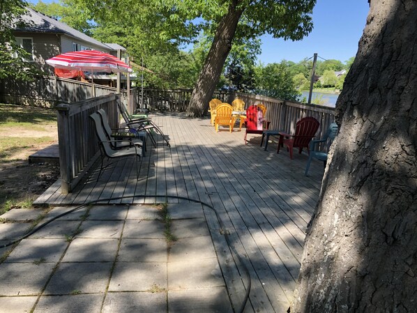 A wooden deck with outdoor furniture, a covered seating area, and a view of a lake. - Dock Life Cottage 10 - Riverside, 2 Bedroom, Wasaga (Wasaga Beach)