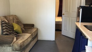 Ett kompakt bostadsutrymme med en soffa, ett litet pentry och en dörr som leder till ett annat rum.